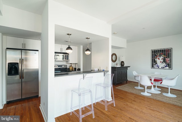 kitchen with a kitchen bar, white cabinetry, appliances with stainless steel finishes, wood finished floors, and dark countertops