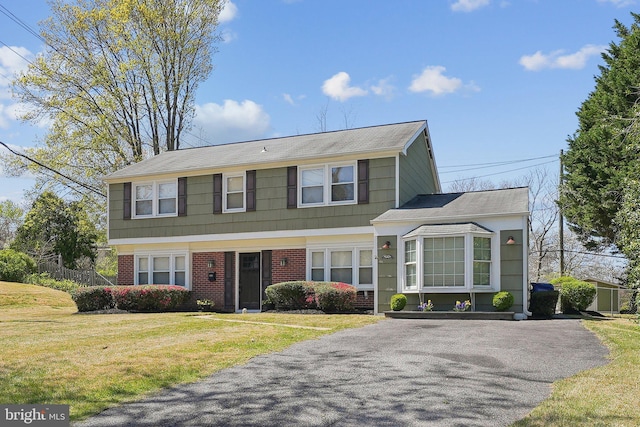 colonial house featuring a front lawn, brick siding, and driveway