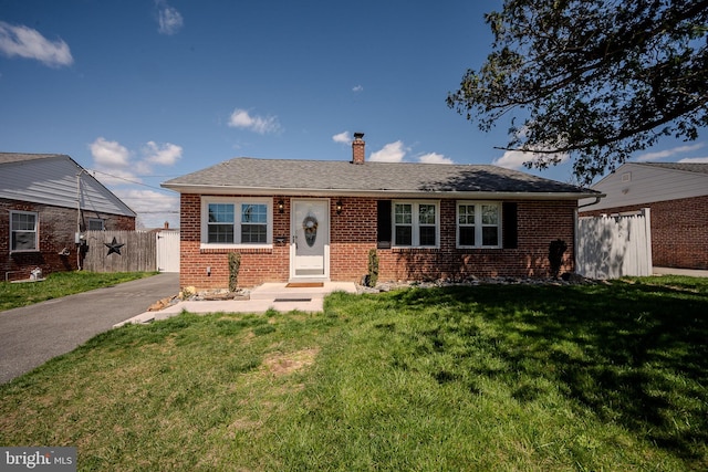 ranch-style house featuring a front yard, a shingled roof, a chimney, fence, and brick siding