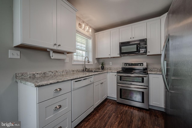 kitchen with a sink, dark wood-style flooring, white cabinetry, stainless steel appliances, and light stone counters