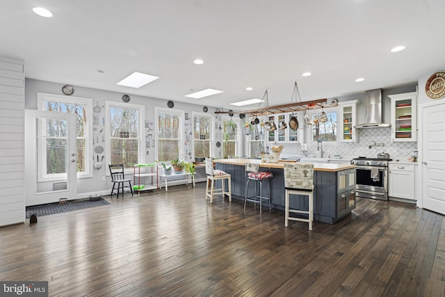 173 Puffball Rd, Hedgesville, WV 25427 - kitchen featuring wall chimney exhaust hood, stainless steel stove, a kitchen bar, white cabinetry, and a skylight