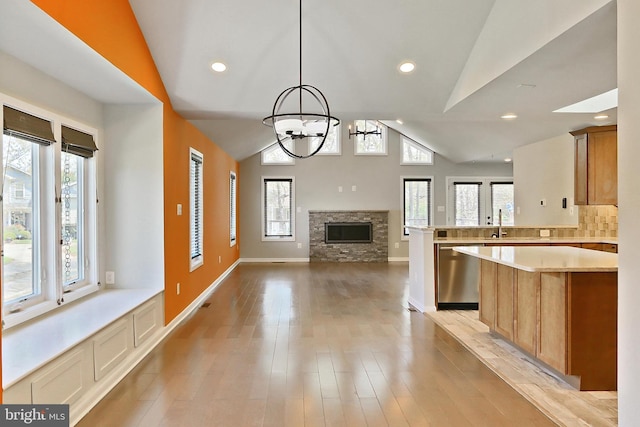 kitchen with a peninsula, vaulted ceiling, dishwasher, light countertops, and a notable chandelier