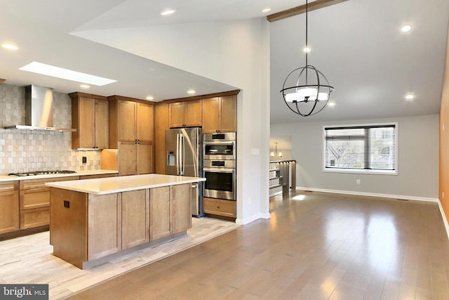 kitchen featuring baseboards, wall chimney range hood, light countertops, appliances with stainless steel finishes, and backsplash