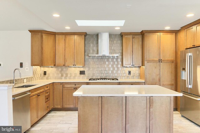 kitchen featuring a sink, wall chimney range hood, decorative backsplash, and appliances with stainless steel finishes