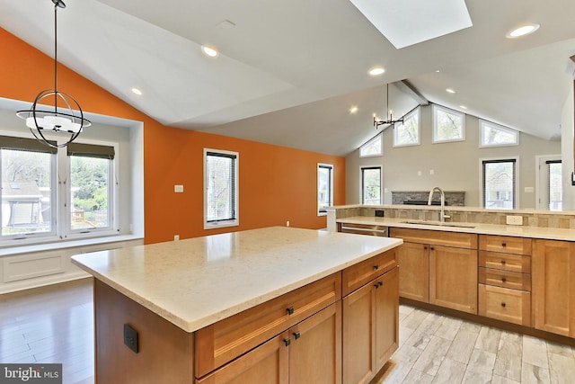 kitchen with vaulted ceiling with skylight, light wood-style flooring, a kitchen island, a sink, and a notable chandelier