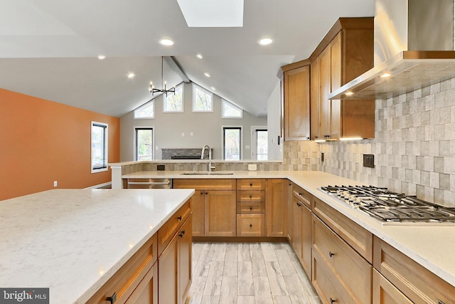 kitchen with vaulted ceiling with skylight, wall chimney range hood, appliances with stainless steel finishes, a sink, and decorative backsplash