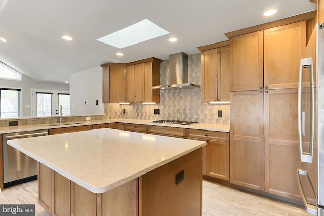 kitchen with a sink, wall chimney range hood, appliances with stainless steel finishes, backsplash, and light stone counters