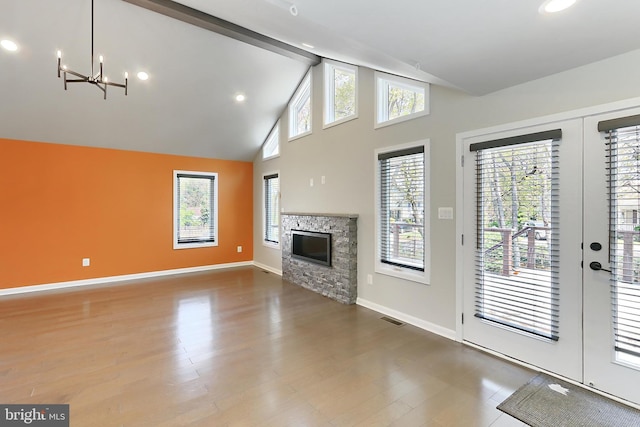 unfurnished living room with high vaulted ceiling, a stone fireplace, visible vents, baseboards, and a notable chandelier