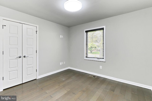 unfurnished bedroom featuring visible vents, baseboards, a closet, and dark wood finished floors