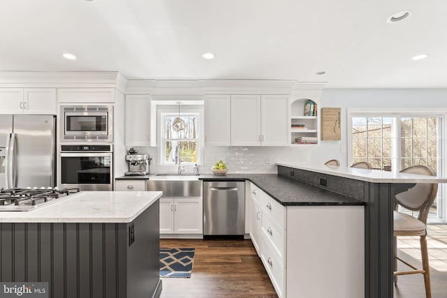 kitchen with a peninsula, open shelves, a breakfast bar area, stainless steel appliances, and a sink