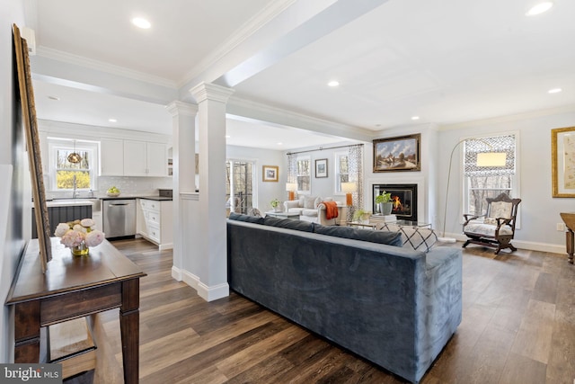 living area featuring a glass covered fireplace, dark wood-type flooring, baseboards, and crown molding