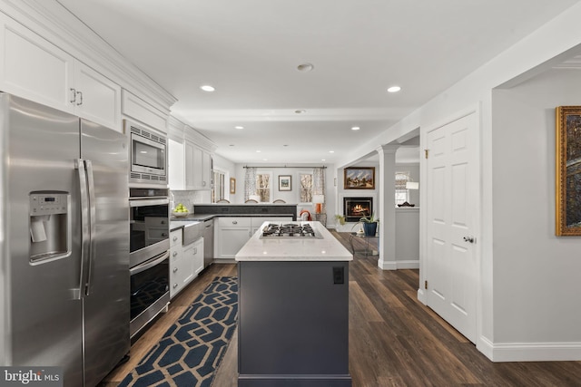 kitchen with dark wood-style flooring, a warm lit fireplace, a center island, white cabinetry, and appliances with stainless steel finishes