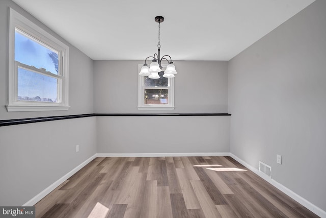 unfurnished room featuring a chandelier, wood finished floors, baseboards, and visible vents