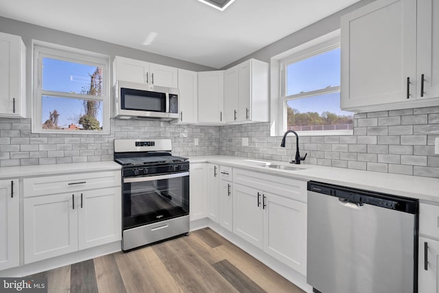 kitchen with a sink, light countertops, appliances with stainless steel finishes, light wood-style floors, and white cabinetry