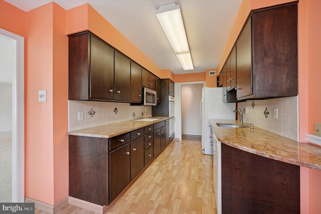 kitchen featuring a sink, stainless steel microwave, light wood-style flooring, dark brown cabinets, and decorative backsplash