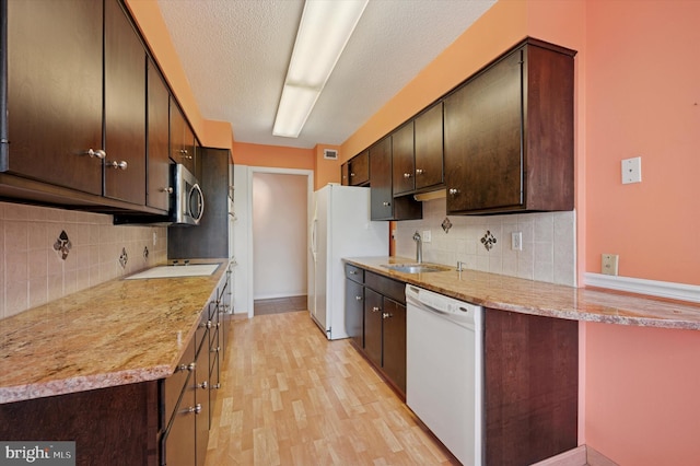 kitchen featuring white appliances, a sink, light wood-type flooring, dark brown cabinets, and a textured ceiling