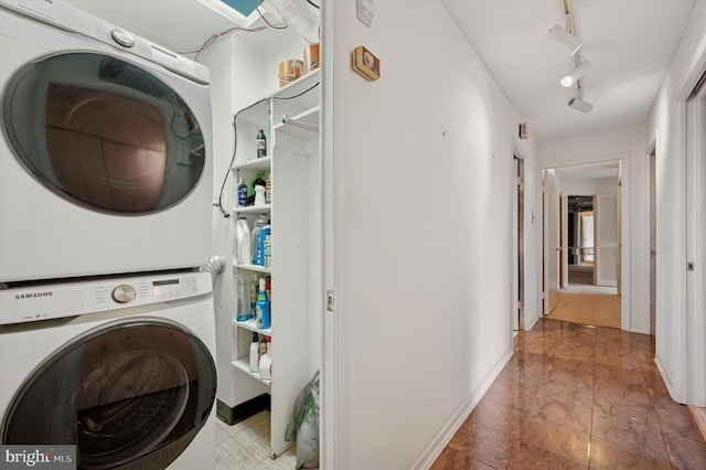 washroom featuring stacked washer / drying machine, rail lighting, and baseboards