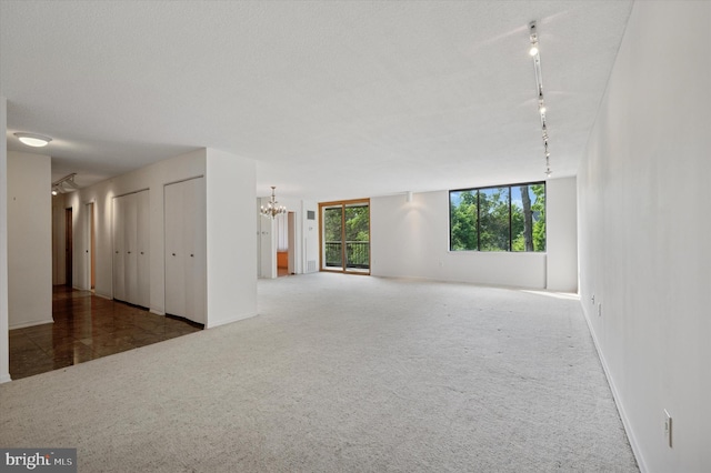 unfurnished living room featuring a chandelier, rail lighting, carpet, and baseboards