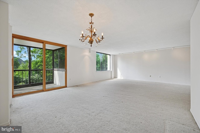 carpeted spare room featuring a chandelier, rail lighting, and baseboards