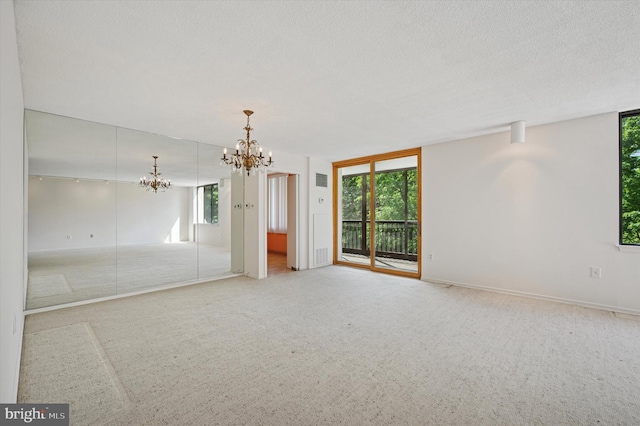 empty room with a chandelier, plenty of natural light, carpet floors, a textured ceiling, and baseboards