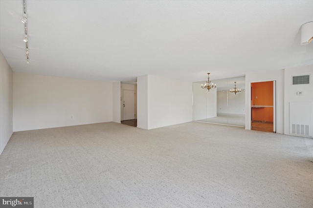 spare room featuring a chandelier, carpet flooring, and track lighting