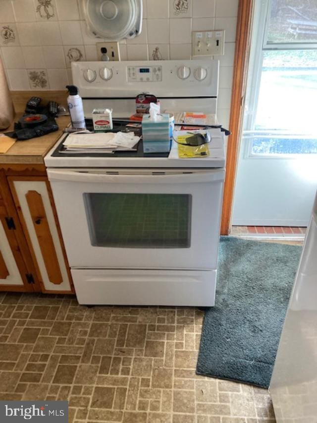 kitchen featuring electric stove, brick floor, light countertops, and decorative backsplash
