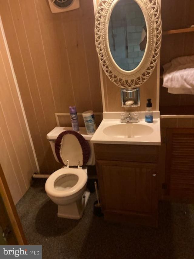 half bathroom with wood walls, vanity, and toilet