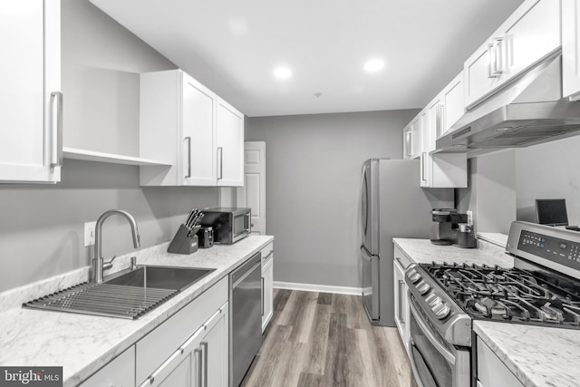 kitchen featuring light stone counters, white cabinetry, under cabinet range hood, stainless steel appliances, and wood finished floors