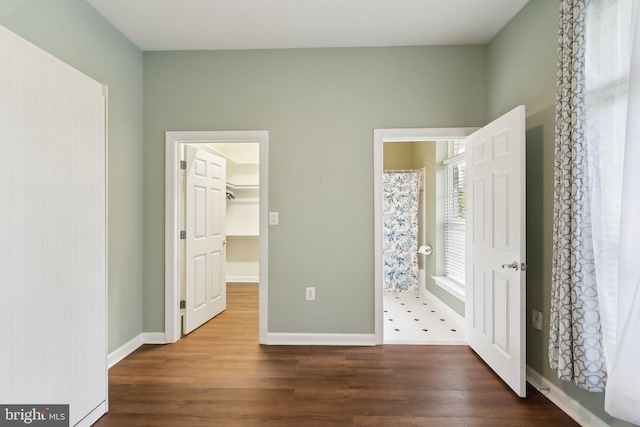 unfurnished bedroom featuring dark wood-type flooring, baseboards, and a walk in closet