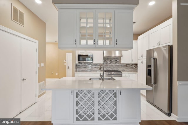 kitchen featuring wall chimney exhaust hood, a sink, visible vents, white cabinetry, and appliances with stainless steel finishes