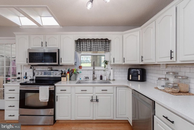 kitchen featuring a sink, a skylight, decorative backsplash, stainless steel appliances, and white cabinets