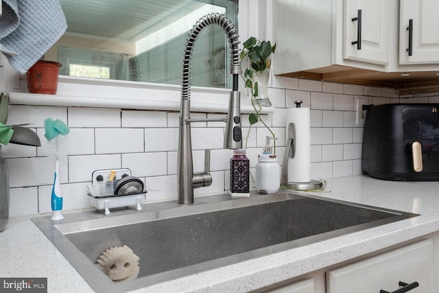 room details with light stone countertops, a sink, backsplash, and white cabinetry