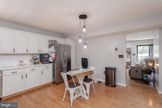 kitchen with hanging light fixtures, decorative backsplash, light wood-type flooring, white cabinetry, and freestanding refrigerator