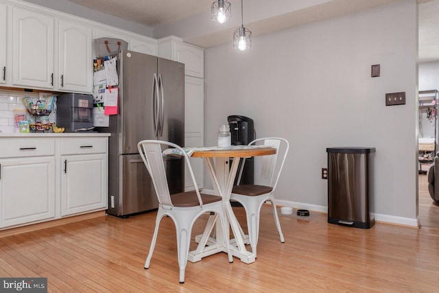 kitchen with light wood-type flooring, baseboards, freestanding refrigerator, and white cabinets
