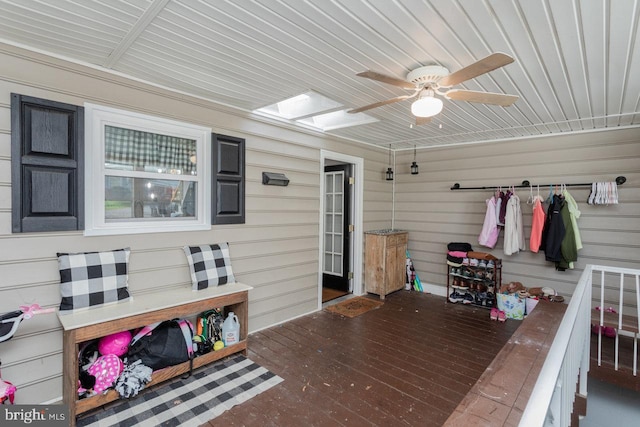exterior space with wood ceiling, a ceiling fan, wooden walls, and a skylight