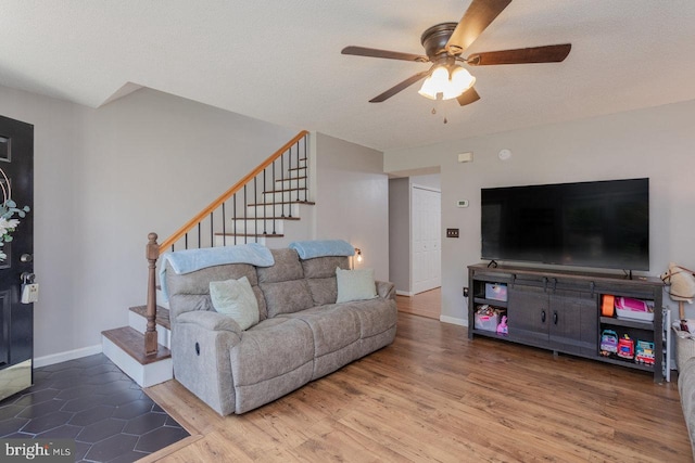 living area featuring stairway, wood finished floors, baseboards, a textured ceiling, and ceiling fan