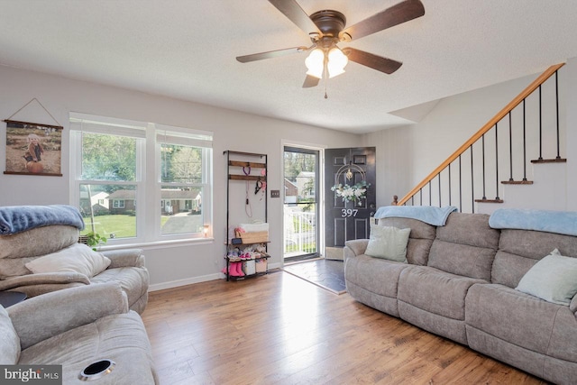 living area featuring stairway, baseboards, a ceiling fan, and wood finished floors
