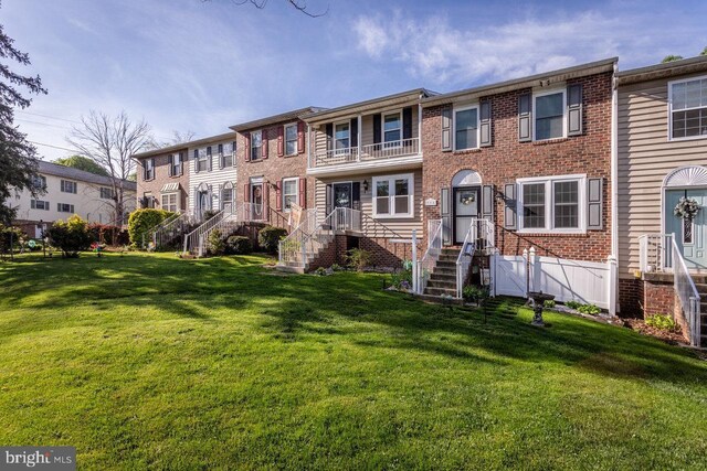 multi unit property with brick siding, a front yard, and a balcony