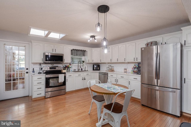 kitchen with a skylight, stainless steel appliances, light countertops, and white cabinetry