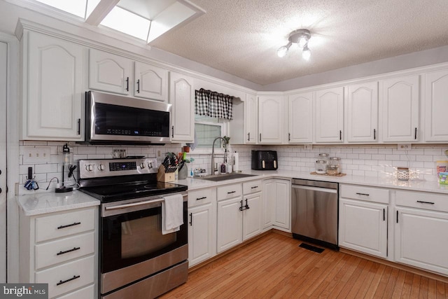 kitchen with white cabinets, a sink, light wood-style flooring, tasteful backsplash, and appliances with stainless steel finishes