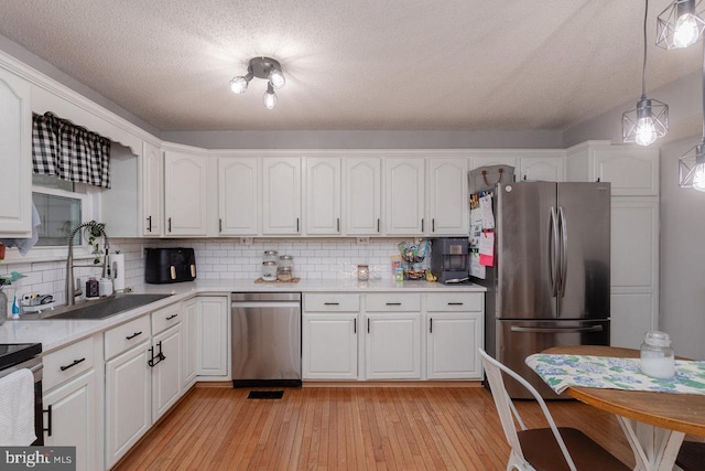 kitchen with stainless steel appliances, a sink, white cabinetry, decorative backsplash, and light countertops