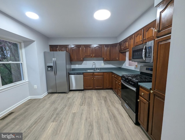 kitchen featuring dark countertops, light wood-style floors, visible vents, stainless steel appliances, and a sink