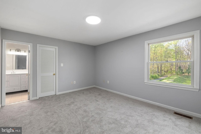 unfurnished bedroom with baseboards, ensuite bath, carpet floors, visible vents, and a sink