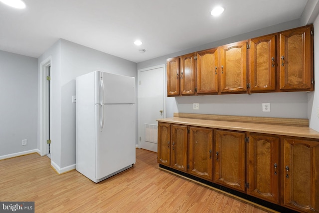 kitchen featuring brown cabinetry, light wood finished floors, light countertops, and freestanding refrigerator
