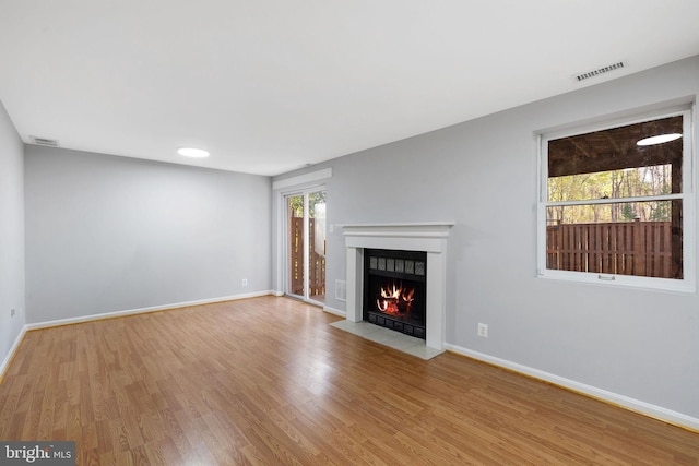 unfurnished living room with visible vents, baseboards, wood finished floors, and a fireplace with flush hearth