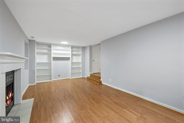 unfurnished living room featuring a fireplace with flush hearth, baseboards, built in features, and light wood finished floors