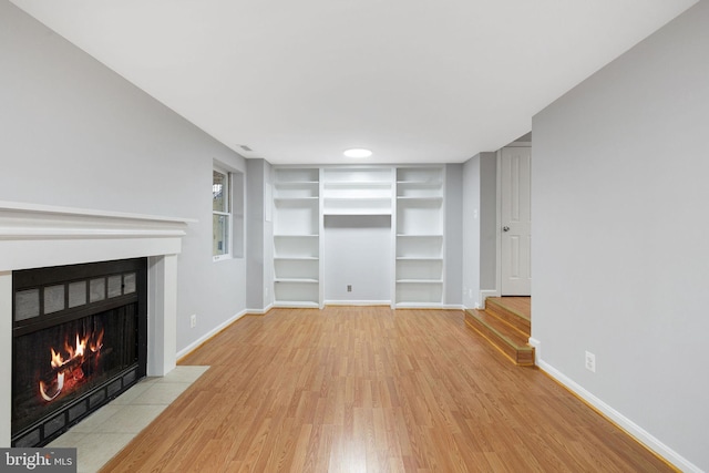 unfurnished living room with built in features, baseboards, light wood-style floors, and a fireplace with flush hearth