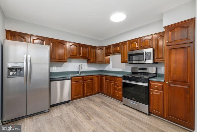 kitchen featuring dark countertops, light wood-type flooring, appliances with stainless steel finishes, and a sink