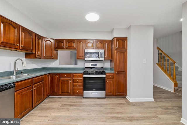 kitchen featuring stainless steel appliances, light wood-type flooring, a sink, and dark countertops