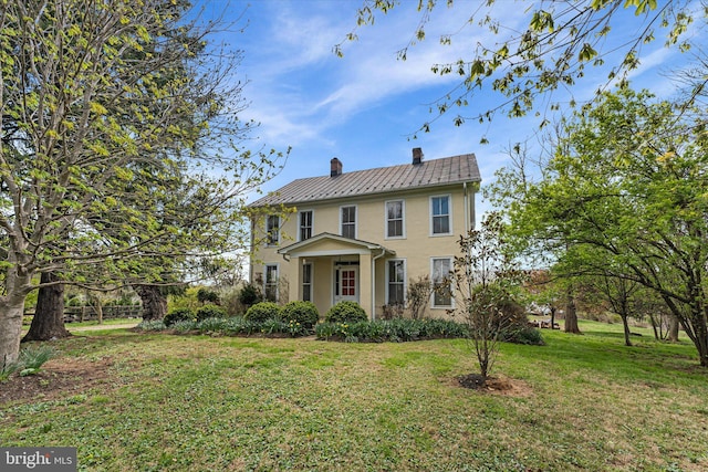 colonial-style house featuring a chimney, stucco siding, and a front lawn